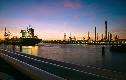 A sea freight vehicle in a panoramic cityscape at dusk with the ExxonMobil Rotterdam refinery in the background.