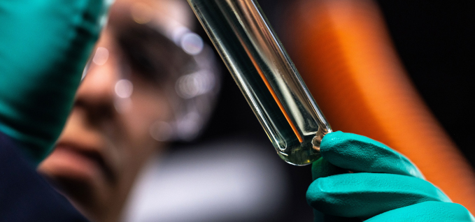 A lab technician wearing safety gloves holding the results of an experiment in a vial.