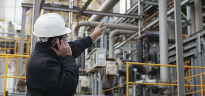 An ExxonMobil engineer points at refinery while on a phone call.
