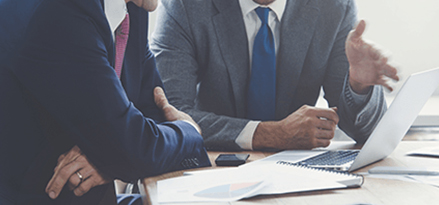 Two men sit in front of a laptop in a business meeting