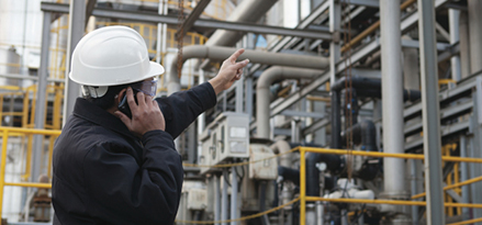 An ExxonMobil engineer points at refinery while on a phone call.