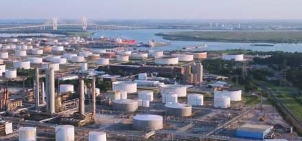 Aerial view of an oil refinery with large storage tanks near a river and bridge.
