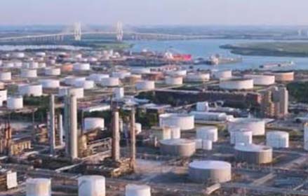 Aerial view of an oil refinery with large storage tanks near a river and bridge.