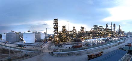 Panoramic view of a refinery at dusk with storage tanks and lit industrial towers.