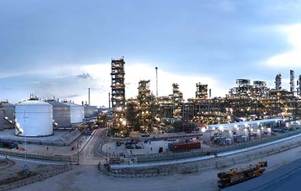 Panoramic view of a refinery at dusk with storage tanks and lit industrial towers.