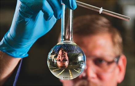 Scientist looking at clear liquid in a flask
